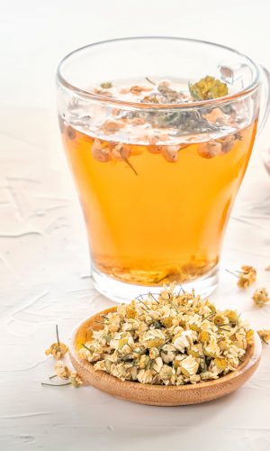 Herbal tea with pharmaceutical chamomile, dry chrysanthemum and hunters on a white table. Copy space