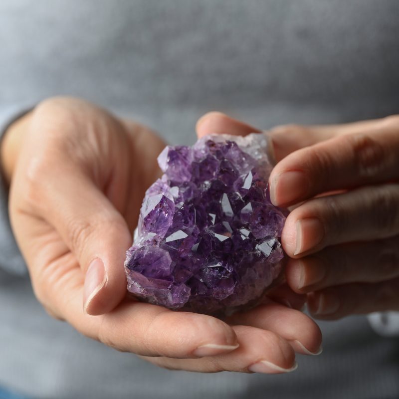 Woman holding beautiful violet amethyst gemstone, closeup