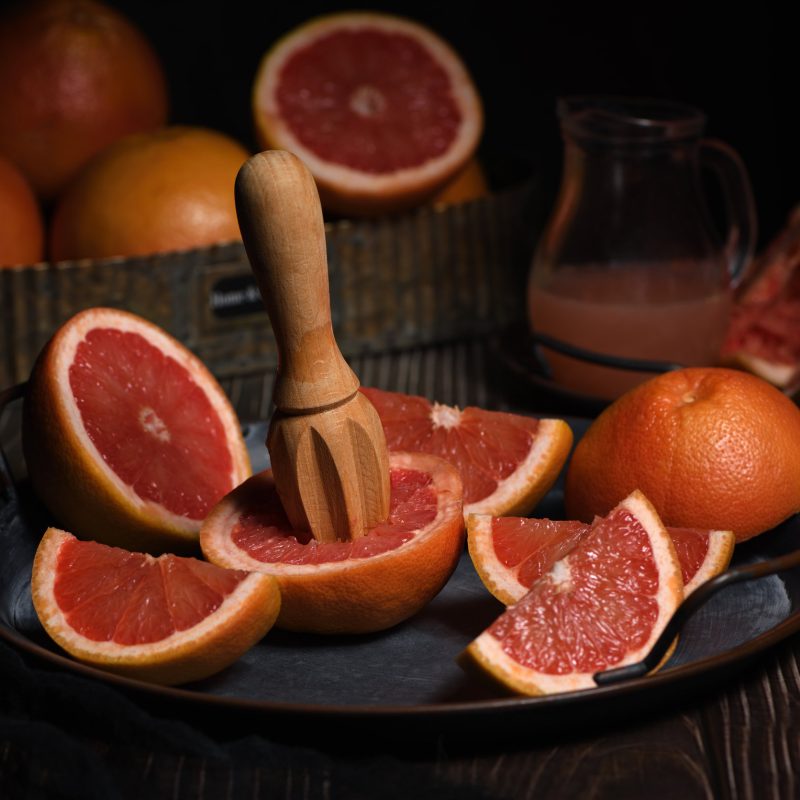 Slices of fresh grapefruit prepared for making fresh squeezed juice on a platter, dark background