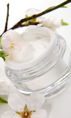 Closeup of jar of moisturizing face cream surrounded by almond flowers
